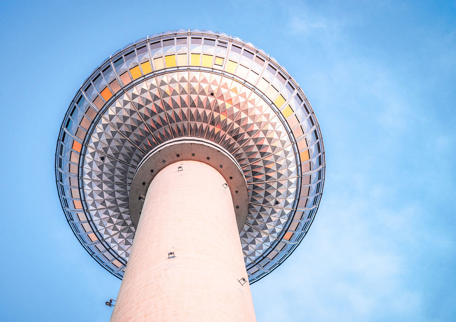 Berliner Fernsehturm aus der Untersicht vor blauem Himmel, mit Spiegelungen in den Fenstern.